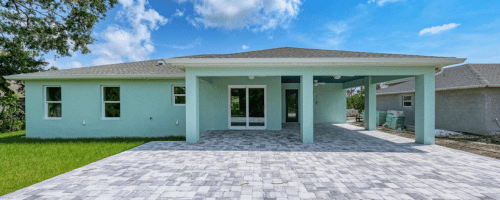 Englewood home renovation showcasing a newly constructed light blue house with a spacious paver patio and modern design elements, emphasizing Florida charm and outdoor living.